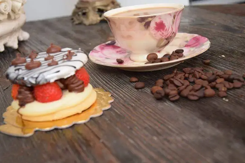 شیرینی لادن طلایی: دسر جذاب توت فرنگی و شکلات در کنار فنجان قهوه معطر و دانه های تازه قهوه روی میز چوبی زیبا.