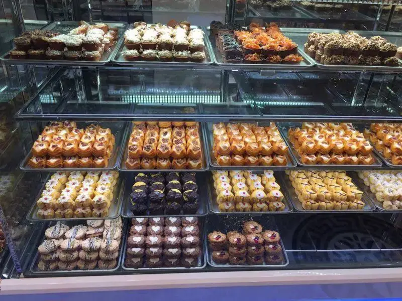 ویترین مغازه شیرینی لادن طلایی با مجموعه‌ای رنگارنگ از شیرینی‌جات تازه و لذیذ، از جمله انواع کوکی، تارت و باقلوا.