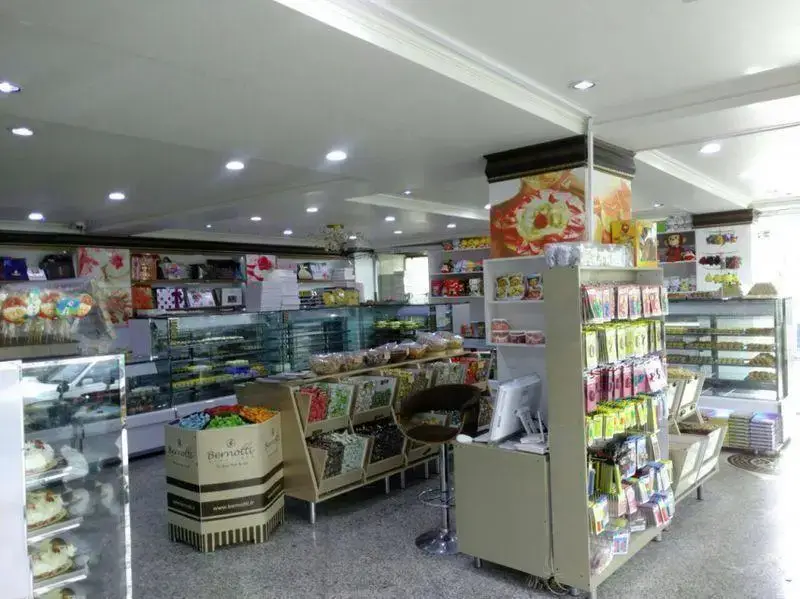 نمای داخلی شیرینی لادن طلایی با ویترین‌های پر از کیک و شیرینی، انواع آجیل، شکلات و محصولات Bernotti. محیطی دلنشین برای خرید.