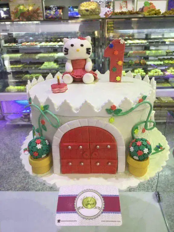 کیک تولد دخترانه هلو کیتی، مناسب یک سالگی، طراحی قلعه‌ای زیبا از شیرینی لادن طلایی، بهترین انتخاب برای جشن‌های کودکانه.