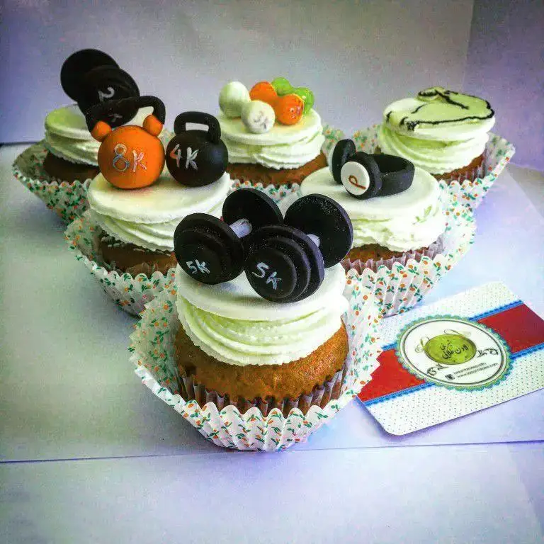 کاپ کیک‌های فانتزی شیرینی لادن طلایی با تزیینات تم ورزشی، شامل دمبل، وزنه، کتل بل و هدفون، برای ورزشکاران.