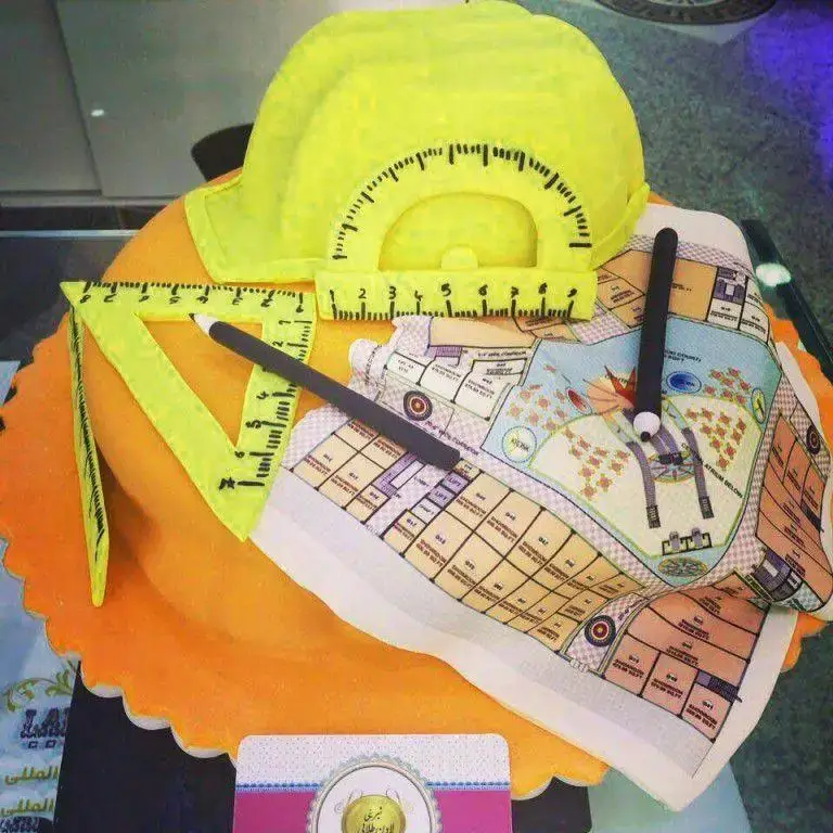 کیک مهندسی خاص شیرینی لادن طلایی شامل کلاه زرد، نقاله، گونیا و نقشه‌های معماری با قلم، ایده‌آل برای مراسم.