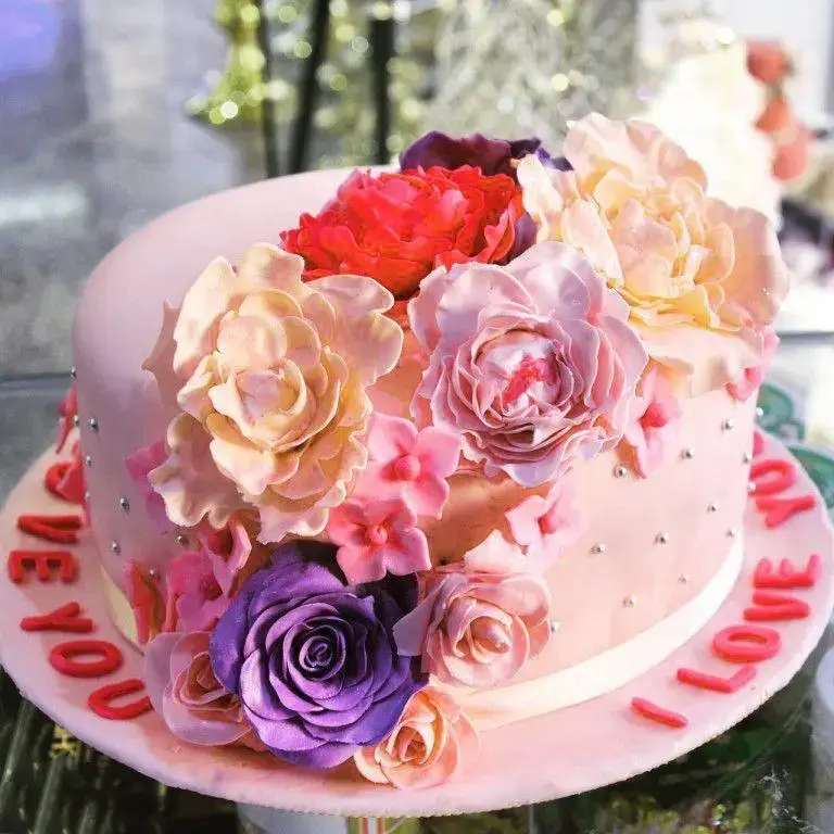 کیک تولد و سالگرد صورتی بسیار زیبا از شیرینی لادن طلایی، مزین به گل‌های شکری متنوع و پیغام "دوستت دارم" برای سورپرایز عزیزان.