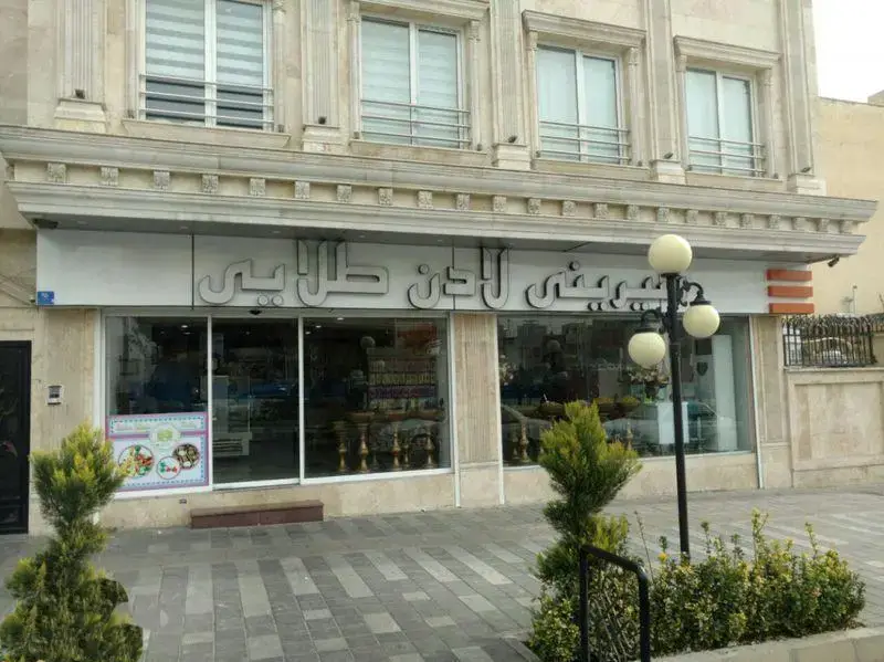 نمای بیرونی جذاب شیرینی لادن طلایی، یک قنادی بزرگ و لوکس با تابلو و ویترین‌های پر از شیرینی و دسر.