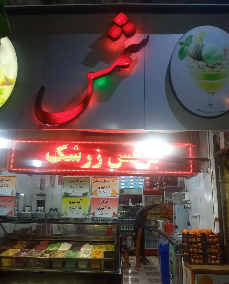 عکس مغازه آبمیوه و بستنی شمس، با تابلو نئون قرمز، دکوراسیون داخلی جذاب، بستنی‌های رنگارنگ و آبمیوه‌های تازه طبیعی.
