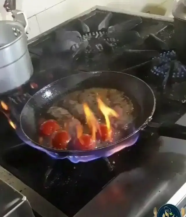 غذایی خوش‌طعم در حال شعله‌ور شدن در تابه روی اجاق گاز حرفه‌ای، هنر آشپزی رستوران کترینگ پریزاد را به نمایش می‌گذارد.