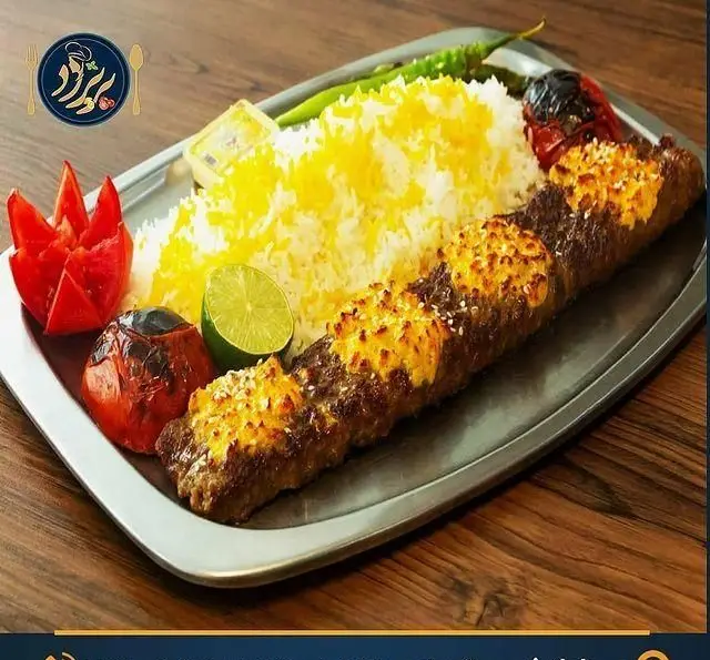 غذای لذیذ ایرانی: کباب کوبیده خاص با رویه طلایی و برنج زعفرانی خوش‌عطر، همراه با گوجه کبابی و فلفل سبز تازه، آماده شده در رستوران کترینگ پریزاد