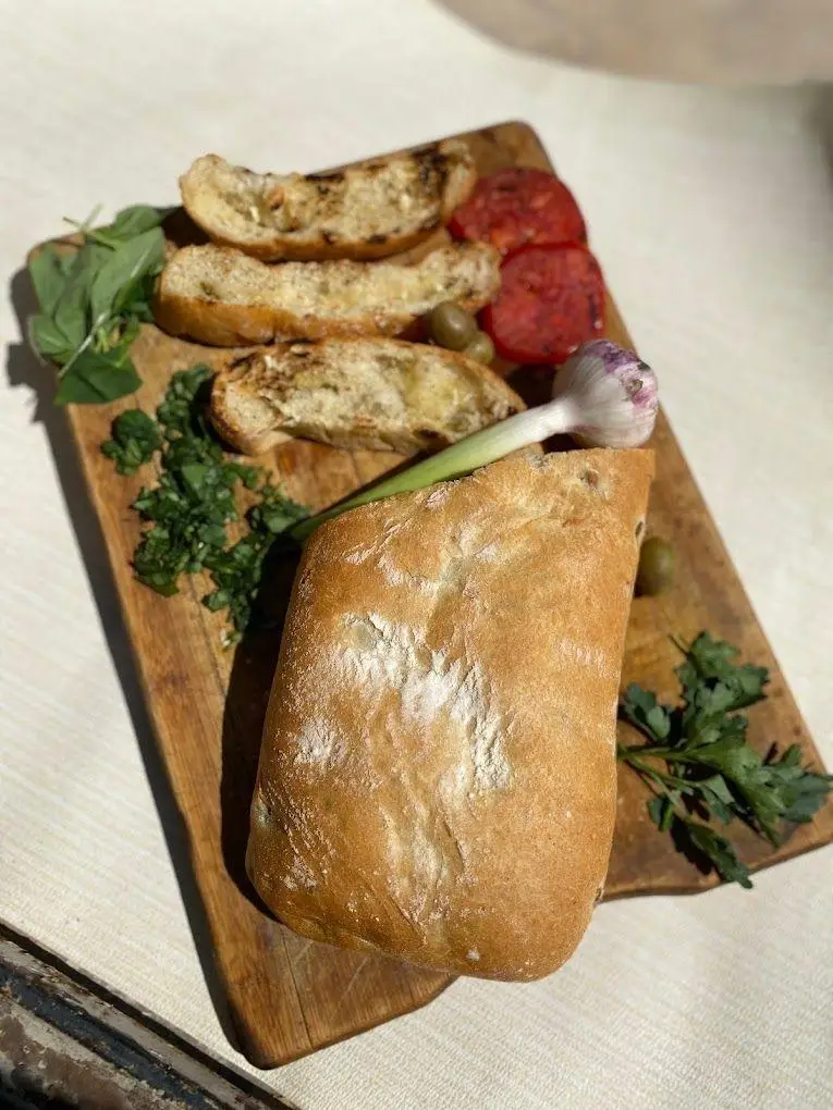 تخته چوبی با نان تازه، گوجه کبابی، سیر، زیتون، ریحان و جعفری، مناسب برای وعده سالم در رستوران رژیمی گیاهی تیم فیت.