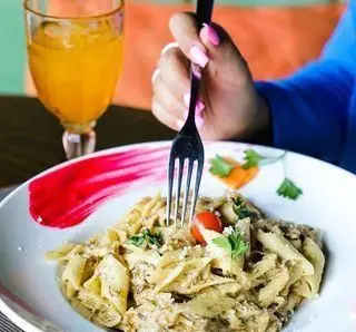 مشتری با لذت در حال میل کردن پاستای خامه‌ای مخصوص ویند در رستوران ایتالیایی ویند، همراه با نوشیدنی تازه. تجربه غذایی دلپذیر.