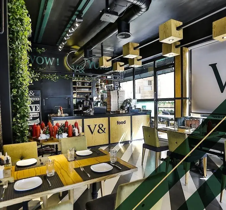 دکوراسیون شیک و سبز رستوران ایتالیایی ویند، فضای مدرن با میزهای چوبی، سقف سیاه و کف شطرنجی، مکانی عالی برای تجربه غذای ایتالیایی.