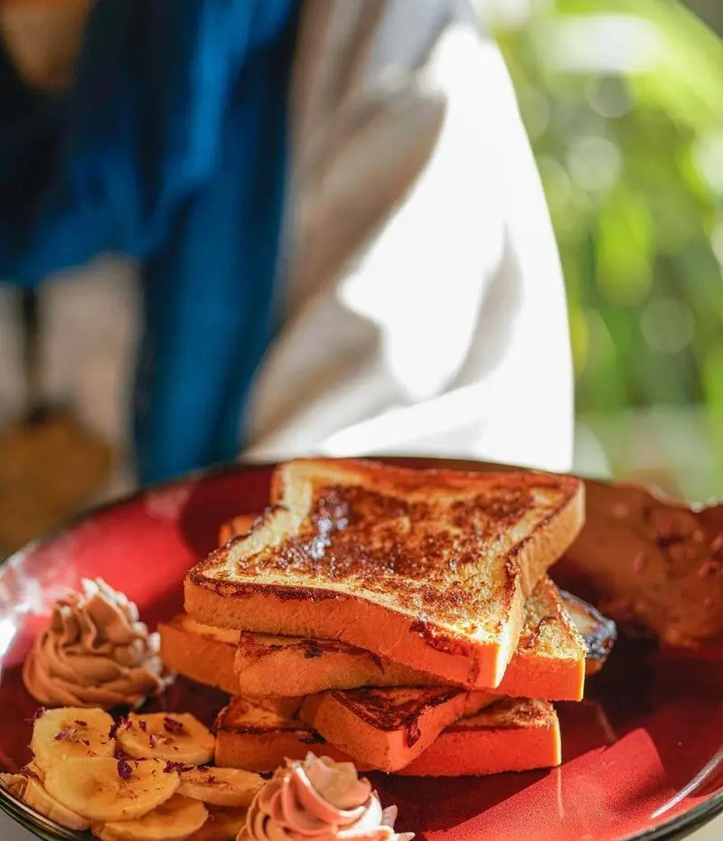 صبحانه لذیذ کافه رستوران بابل: فرنچ تست طلایی با موز و خامه فرم گرفته، تزئین شده با گل محمدی در فضایی دلنشین و آفتابی.