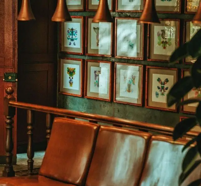 دکوراسیون شیک و هنری کافه رستوران بابل با دیواری از تابلوهای مدرن، مبلمان چرمی راحتی و آویزهای مسی خاص.