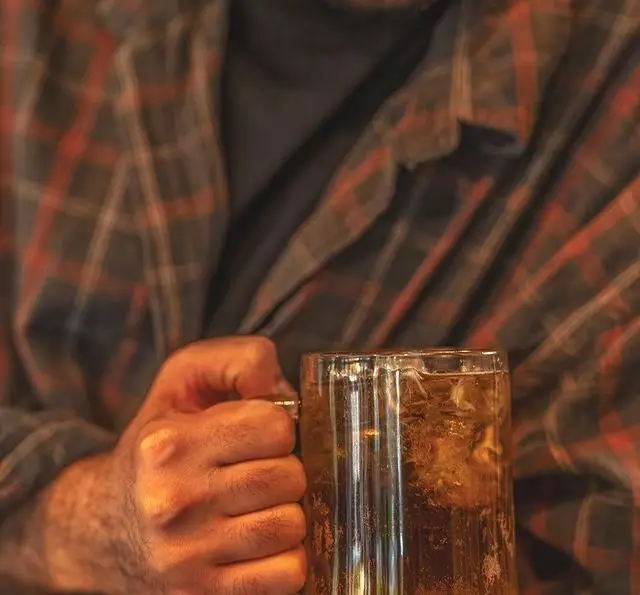 مشتری با پیراهن چهارخانه، لیوان ماگ نوشیدنی سرد و گوارا در دست در کافه رستوران بابل. لذت طعم دلپذیر در محیطی آرام.