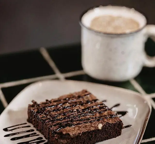 براونی شکلاتی و مغزدار با تزئین سس شکلات، همراه با یک فنجان قهوه لذیذ در کافه رستوران بابل.