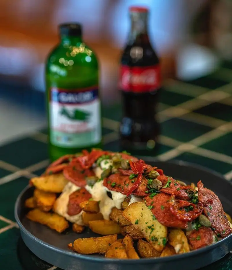 نمایی از سیب زمینی تنوری با سس، گوجه خشک و کاپاریس، یک تجربه خوشمزه در کافه رستوران بابل، همراه با نوشیدنی.