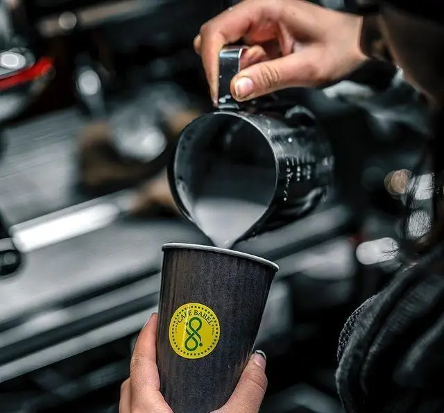 تصویری از باریستا در کافه رستوران بابل هنگام ریختن شیر فوم‌دار برای لاته یا کاپوچینو در فنجان بیرون‌بر برند کافه بابل.