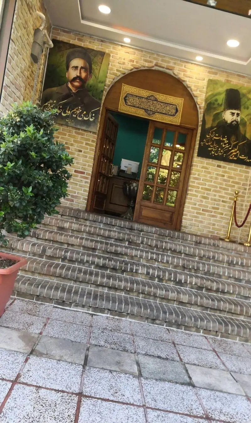 ورودی باشکوه رستوران مرشد سعادت آباد با دیوارهای آجری، پله‌های زیبا و تابلوهای پرتره بزرگان فرهنگ ایرانی.