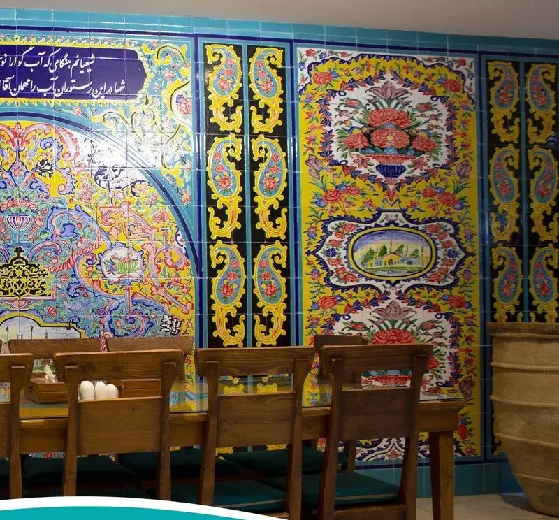 دکوراسیون داخلی رستوران مرشد سعادت آباد با کاشی‌کاری‌های سنتی ایرانی، نقوش رنگارنگ گل و مرغ و بته‌جقه، میز و صندلی چوبی در محیطی دلنشین.