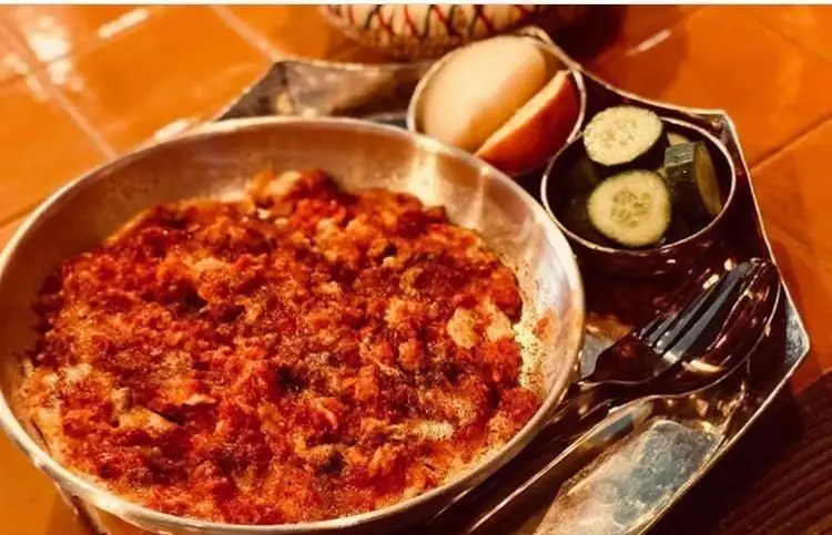 صبحانه خوشمزه رستوران رافی: املت گوجه فرنگی داغ در تابه، با برش‌های خیار تازه و میوه، سرو شده روی سینی فلزی شیک و جذاب