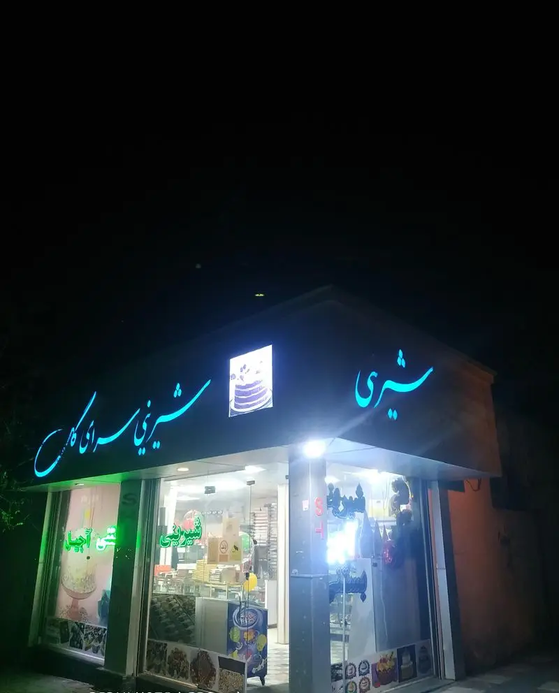 قنادی گل (مجید) در شب، تابلوی نئون آبی 'شیرینی سرای گل گیس' درخشان، ویترین پرنور با انواع کیک و شیرینی تازه.