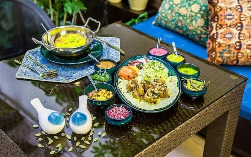 میز غذا در رستوران رزفر با سینی کباب و پلو، خورشت زرد، کاسه‌های مخلفات رنگی و تزئینات هنری در فضایی دلپذیر.