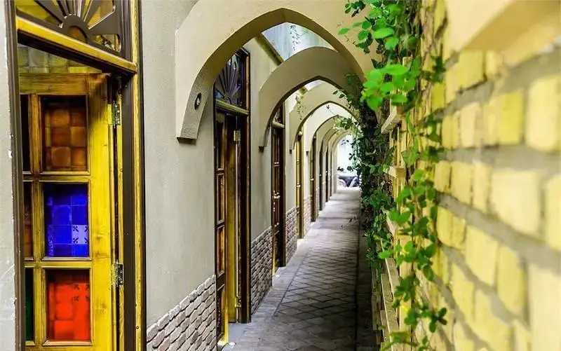 گذرگاه زیبای رستوران رزفر با معماری سنتی ایرانی شامل طاق‌های پی‌درپی، درهای چوبی رنگین و دیوارهای آجری با پوشش گیاهی.