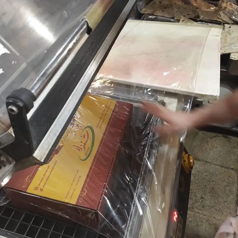 آماده‌سازی و بسته‌بندی بهداشتی جعبه‌های غذای رستوران شنزار با سلفون برای ارسال مطمئن و حفظ کیفیت محصولات.