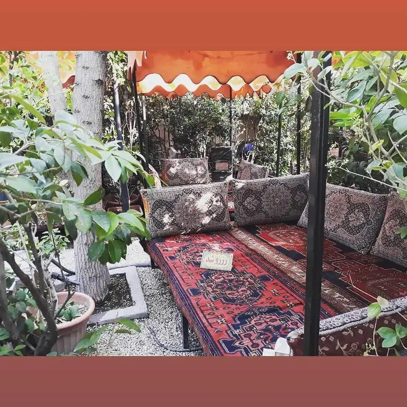 تجربه دلنشین فضای سنتی رستوران شنزار: تخت‌های ایرانی با قالی و بالشتک‌های زیبا، مکانی آرامش‌بخش در میان فضای سبز.