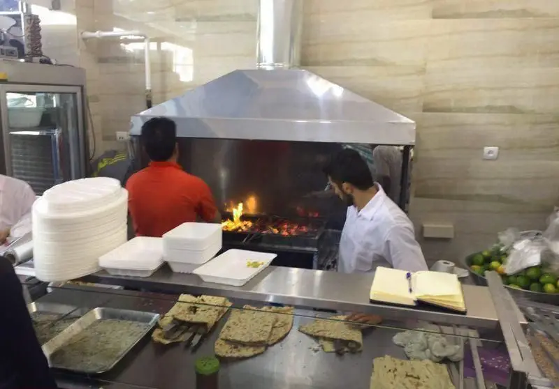 آشپزخانه کباب سرای محسن: پخت کباب‌های اصیل ایرانی بر روی منقل، آماده‌سازی سفارشات با نان تازه و ظروف یکبار مصرف برای مشتریان.