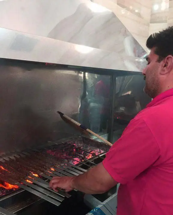 آشپز کباب سرای محسن در حال آماده سازی و پخت کباب کوبیده ایرانی بر روی منقل ذغالی داغ برای مشتریان.