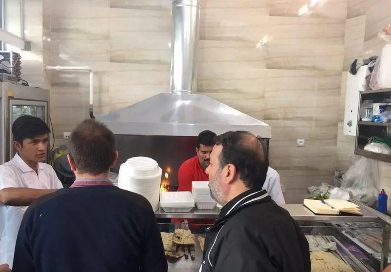 نمایی از کباب سرای محسن، آشپز در حال آماده‌سازی و پخت کباب، حضور مشتریان و کارکنان در فضایی فعال و شلوغ.