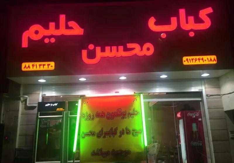 نمای خارجی کباب سرای محسن: تابلوی نئون قرمز "کباب حلیم محسن" و بنر بزرگ حلیم بوقلمون، با شماره تماس 09124690188 و 88413330.