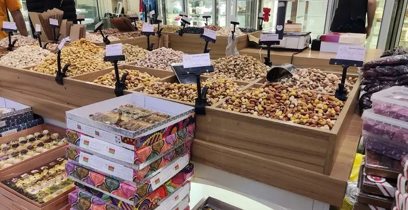 نمایش متنوع آجیل و خشکبار مرغوب در ظروف چوبی فروشگاه شیرینی مانلی تهرانپارس، همراه با بسته‌های شیرینی خوشمزه.