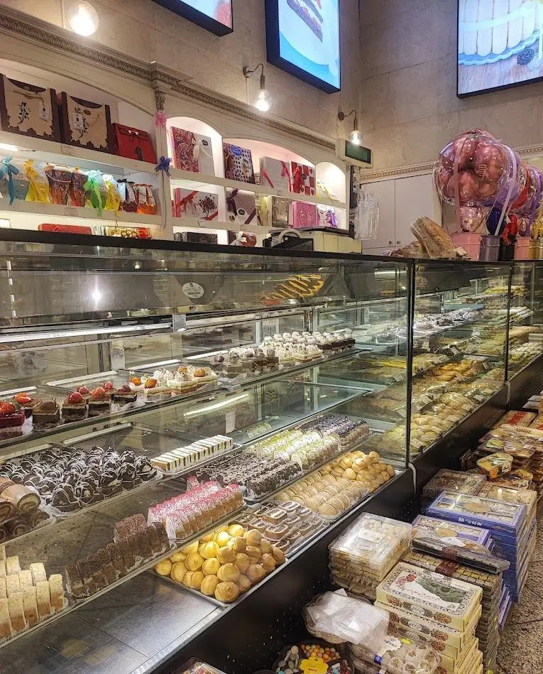 شیرینی‌فروشی مانلی تهرانپارس، نمایشگر ویترین‌های پربار انواع کیک، شیرینی، باقلوا، دسر و بسته‌های هدیه جذاب برای مشتریان.
