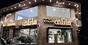 نمای خارجی روشن و جذاب شیرینی مانلی تهرانپارس در شب. یک قنادی و شیرینی فروشی مدرن با دیوارهای آجری و نورپردازی حرفه‌ای.