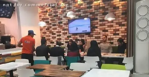 فضای داخلی دنج و مدرن فست فود سیتادو با دیوار آجری و تلویزیون. مشتریان در حال صرف غذا و پرسنل آماده سرویس‌دهی.