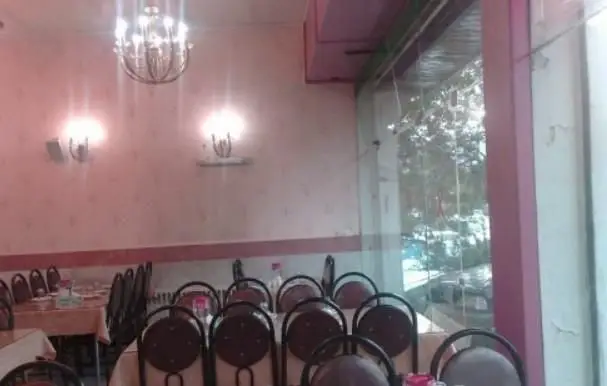 نمایی از فضای داخلی رستوران ایرانی اقدسیه؛ شامل میز و صندلی‌های مرتب، لوستر و چراغ‌های دیوارکوب و پنجره‌ای با دید فضای سبز.