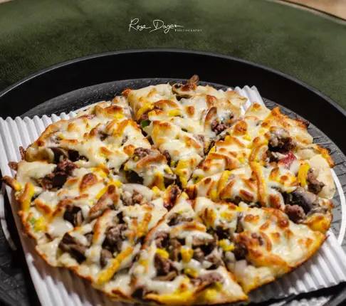 پیتزای جذاب و خوش‌رنگ و لعاب کافه پستو با تاپینگ‌های گوشت، قارچ و ذرت طلایی، ایده‌آل برای یک تجربه غذایی فوق‌العاده.