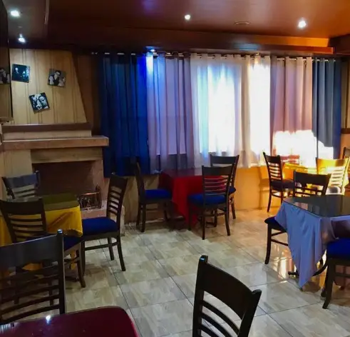 فضای داخلی دنج و دلنشین کافه پستو با میز و صندلی‌های چوبی آبی و قرمز، شومینه و پرده‌های رنگی. محیطی گرم و آرام برای مشتریان.