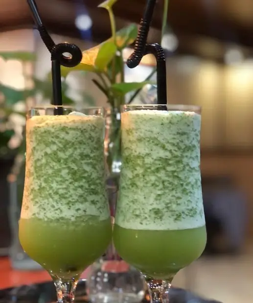 دو لیوان اسموتی نعنا و لیمو تازه و خنک لایه لایه با نی مشکی در فضای دلنشین کافه پستو، بهترین نوشیدنی تابستانی.