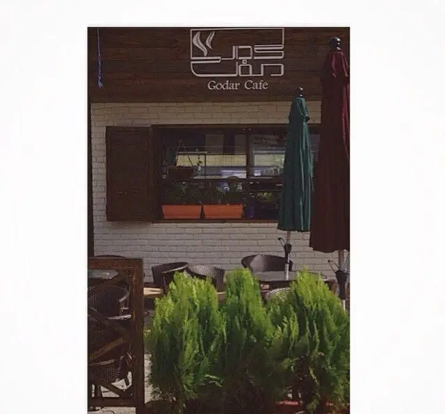 نمایی از فضای بیرونی کافه رستوران گدار، با میز و صندلی‌های شیک، چترهای آفتابگیر و گلدان‌های سرسبز. محیطی دنج برای دورهمی و کافه‌گردی.