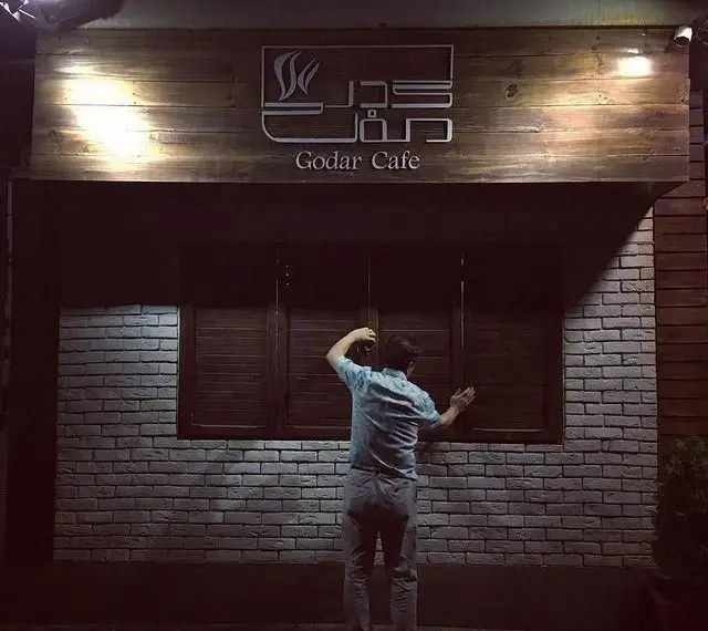 نمای شبانه کافه رستوران گدار با تابلوی چوبی درخشان، آجرکاری شیک و پنجره‌های چوبی بسته.