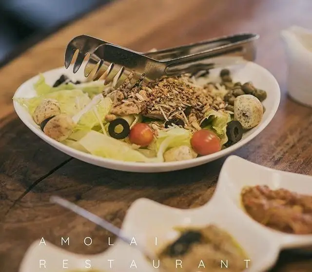 یک کاسه بزرگ سالاد سالم و تازه با کاهو، گوجه گیلاسی، زیتون سیاه، نان سوخاری و دانه های مغذی، آماده سرو با انبر در رستوران آمولای.