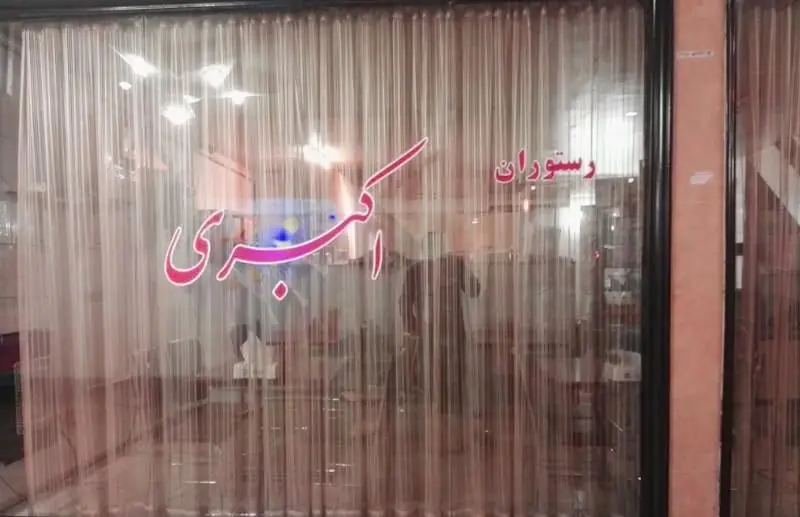 نمای بیرونی و ورودی رستوران ایرانی اکبری با تابلو و نام آن روی شیشه، محلی عالی برای لذت بردن از غذای اصیل و با کیفیت ایرانی.