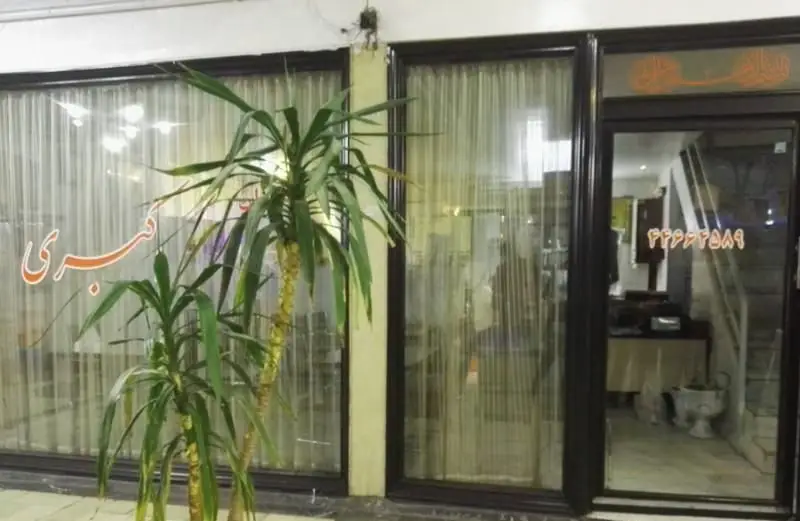 نمای بیرونی رستوران ایرانی اکبری با پنجره‌های شیشه‌ای، پرده‌ها و گیاهان. نام رستوران "اکبری" و شماره تماس ۲۲۶۲۳۶۸۹ در ورودی دیده می‌شود.