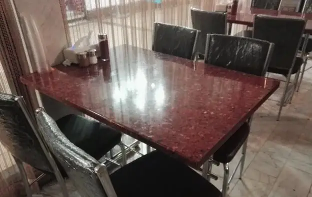 میز غذاخوری شیک و تمیز با رویه گرانیتی و صندلی‌های مدرن در محیط داخلی رستوران ایرانی اکبری، آماده سرو غذاهای لذیذ.