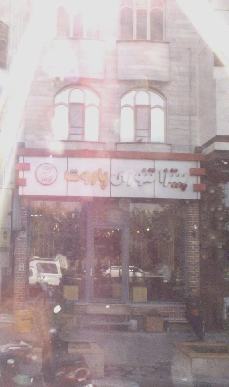 تصویری از نمای خارجی پیتزا تنوری پاروت، یک رستوران با معماری سنتی و تابلوی مشخص در خیابان شلوغ شهری.