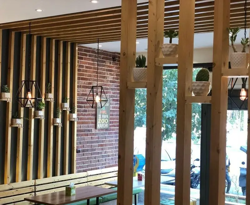 نمای داخلی رستوران پیتزا تنوری پاروت با طراحی مدرن چوبی، گیاهان تزئینی، آویزهای هندسی و دیوار آجری، فضایی دنج برای مشتریان