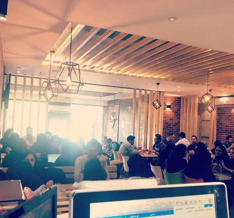 فضای داخلی گرم و صمیمی پیتزا تنوری پاروت با میزهای شلوغ و مشتریانی که از پیتزا تنوری و نوشیدنی‌های خود لذت می‌برند.