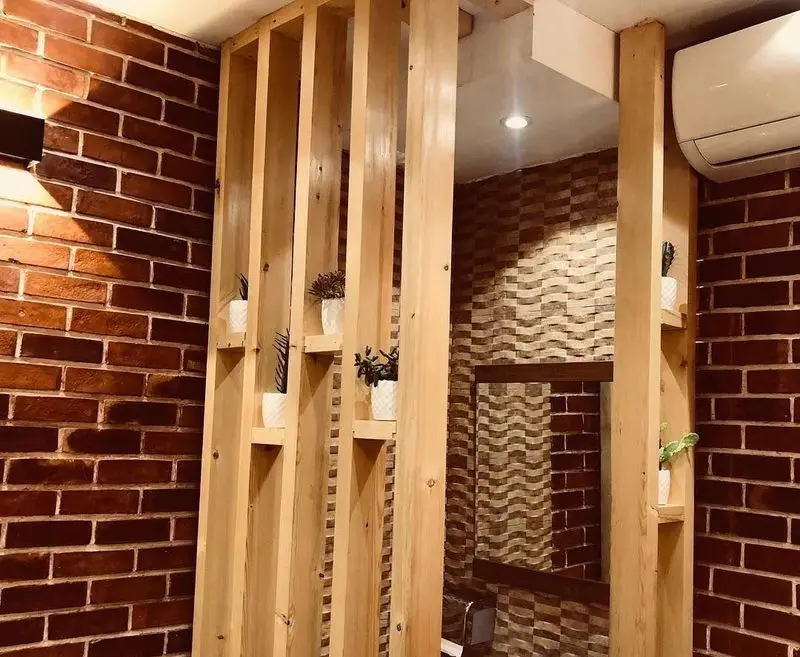 طراحی داخلی جذاب پیتزا تنوری پاروت: دیوارهای آجری، پارتیشن چوبی با گلدان‌های زینتی و آینه، فضایی دلنشین و مدرن.